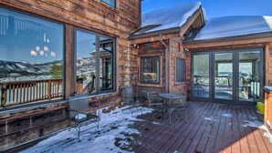 A wooden cabin with large windows, a deck, and a view of a snowy landscape. - Spacious Big Sky Cabin w/ Hot Tub & Grill! (Big Sky)