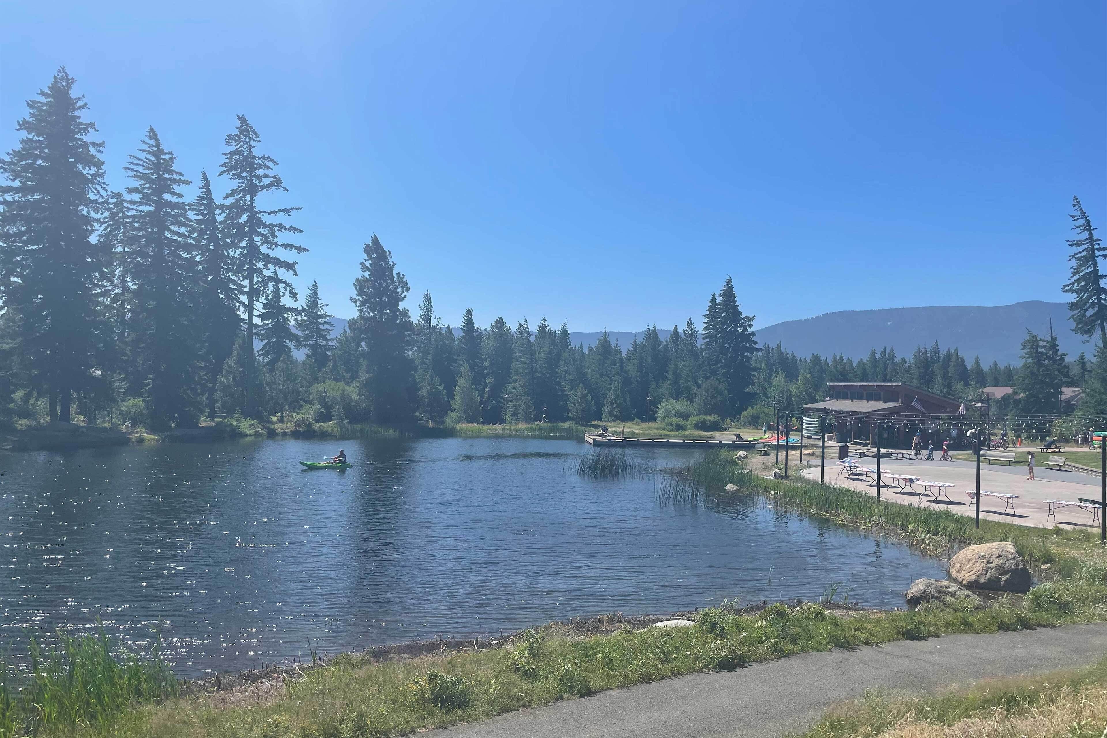 Un lac entouré d’arbres et un parc avec des tables de pique-nique et un bâtiment.