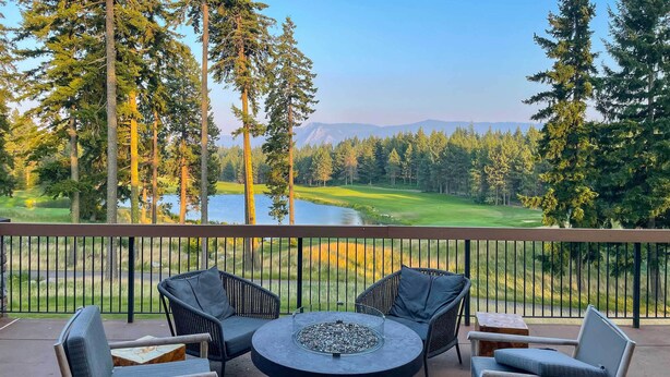 Ein Balkon mit Korbstühlen und einem runden Tisch, mit Blick auf einen Golfplatz und einen See.