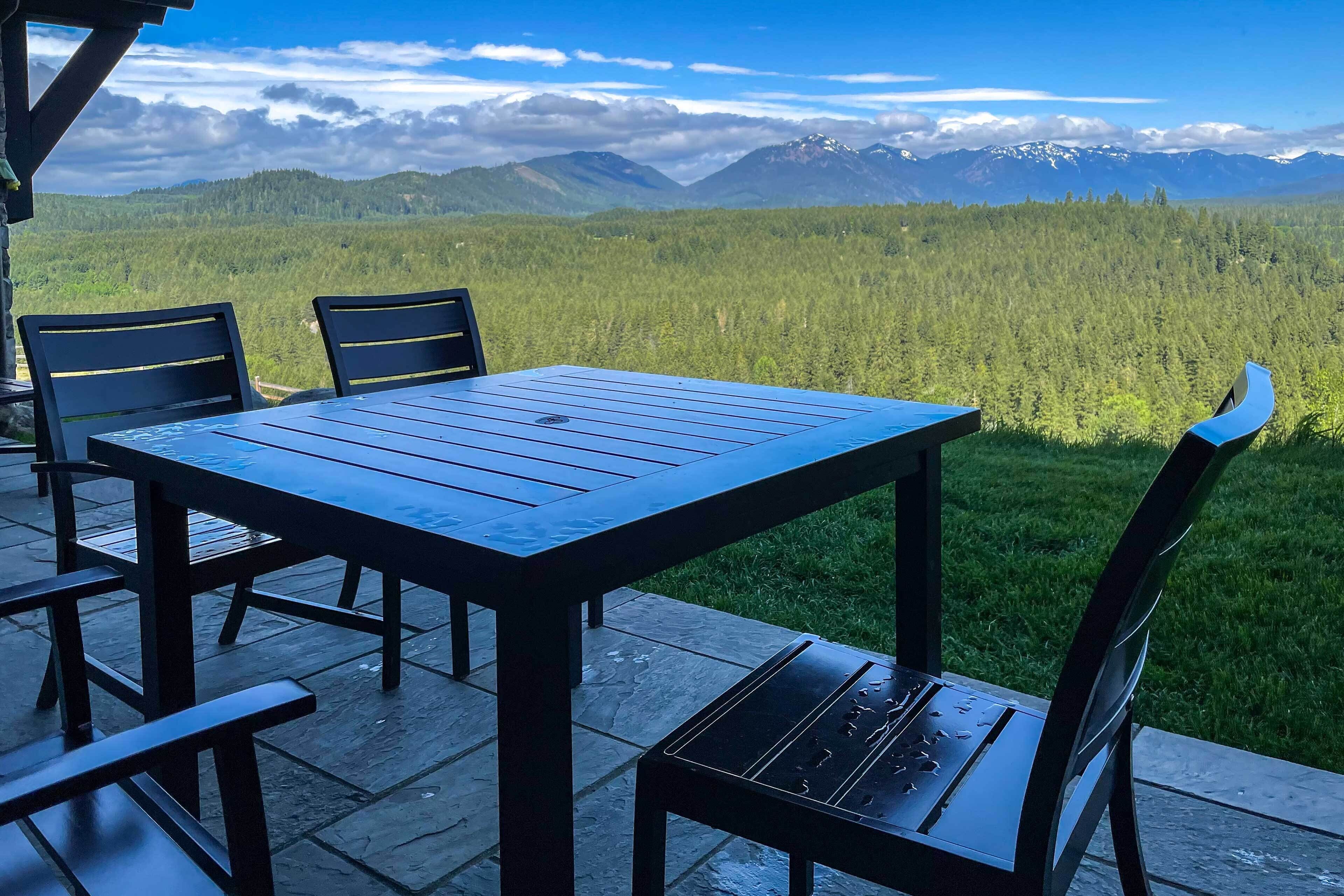 An outdoor seating area with a table and chairs, overlooking a forested mountain range.