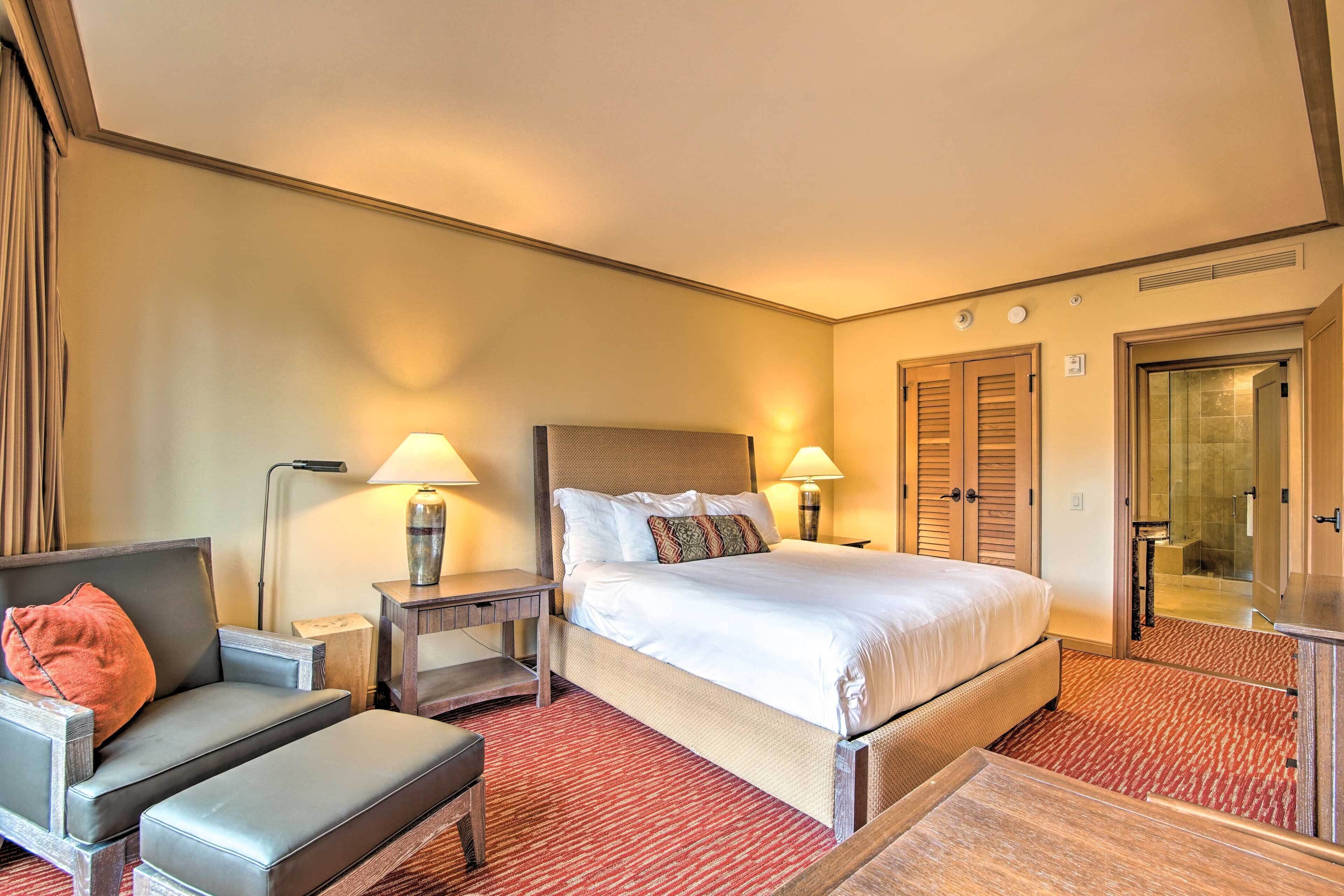 A hotel room with a bed, a chair, a desk, and a lamp.