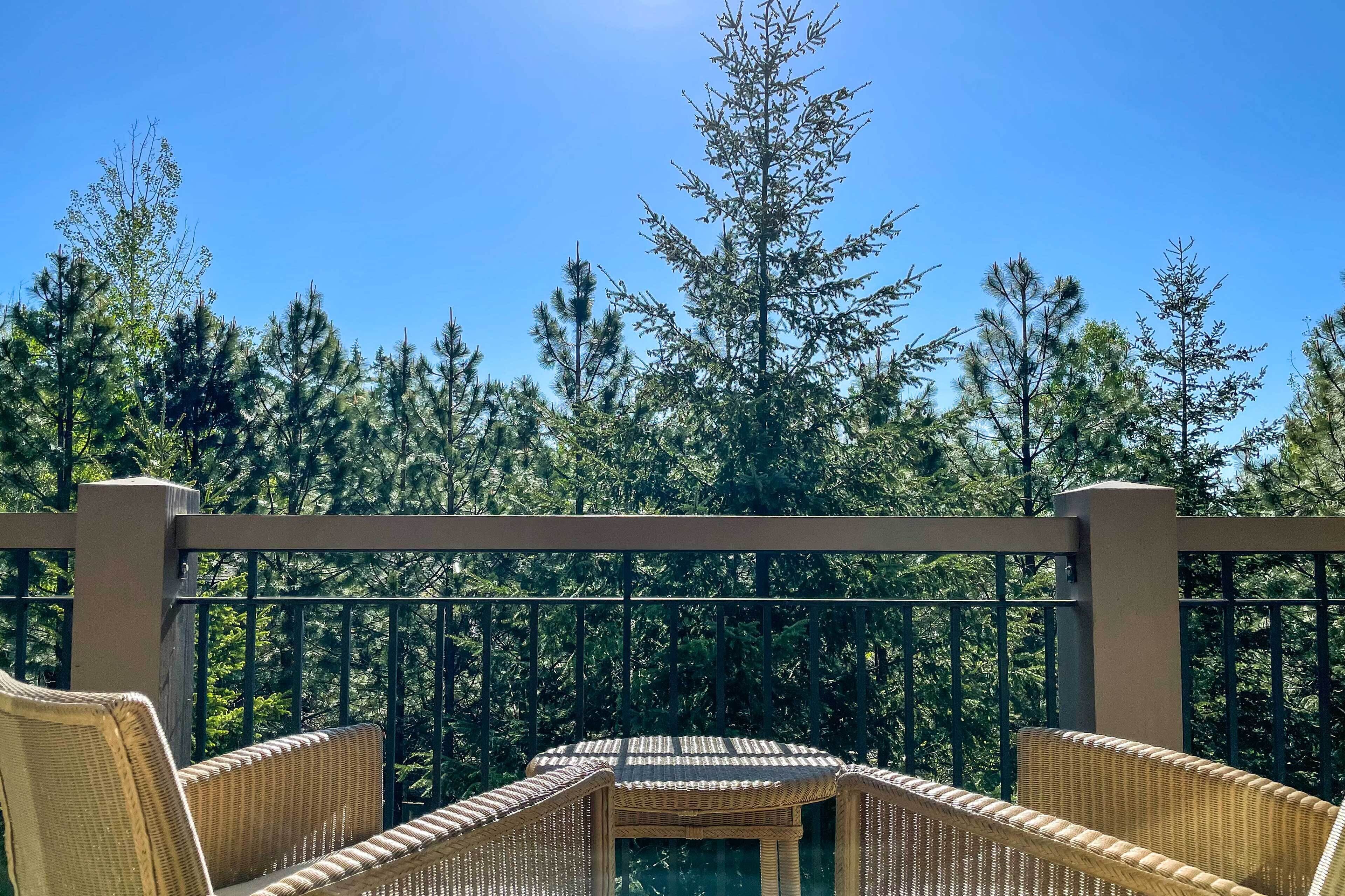 A balcony with wicker furniture and a view of tall trees.