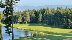 Ein Golfplatz mit Teich, umgeben von Bäumen und Bergen im Hintergrund.