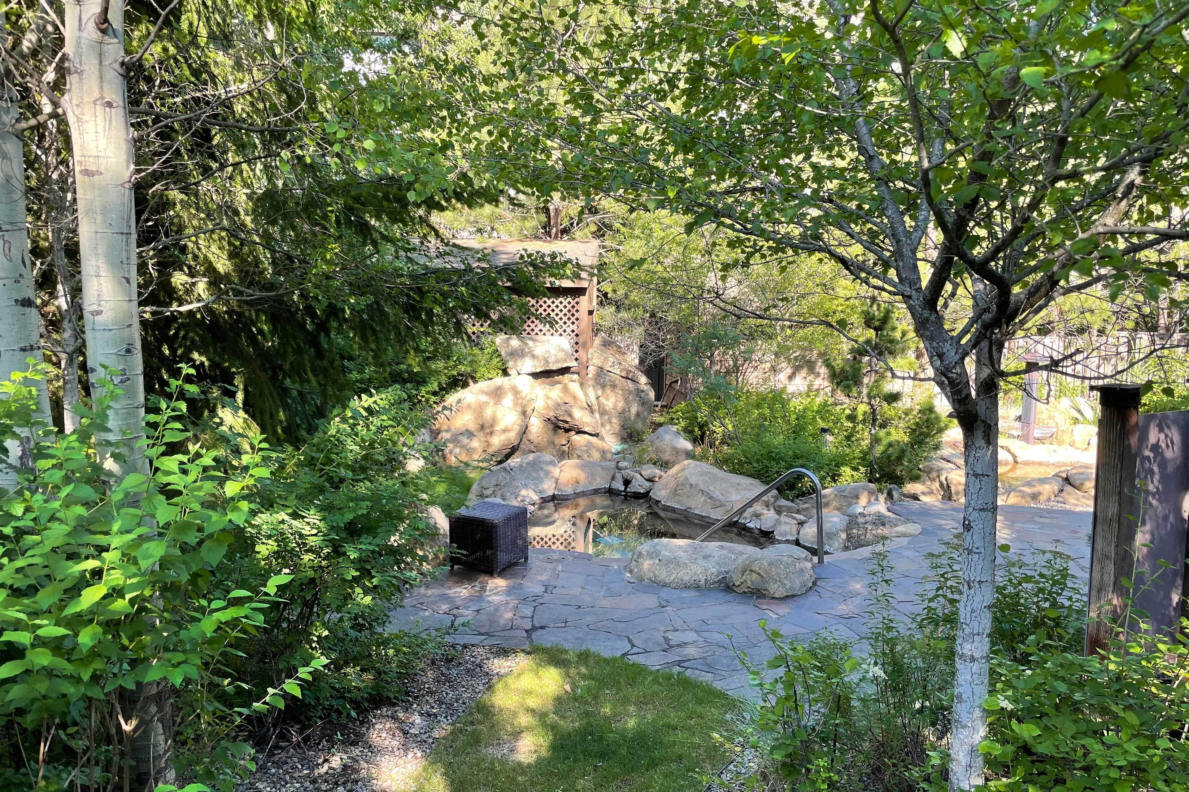 A garden with a stone pathway, a wooden structure, and a rock formation.