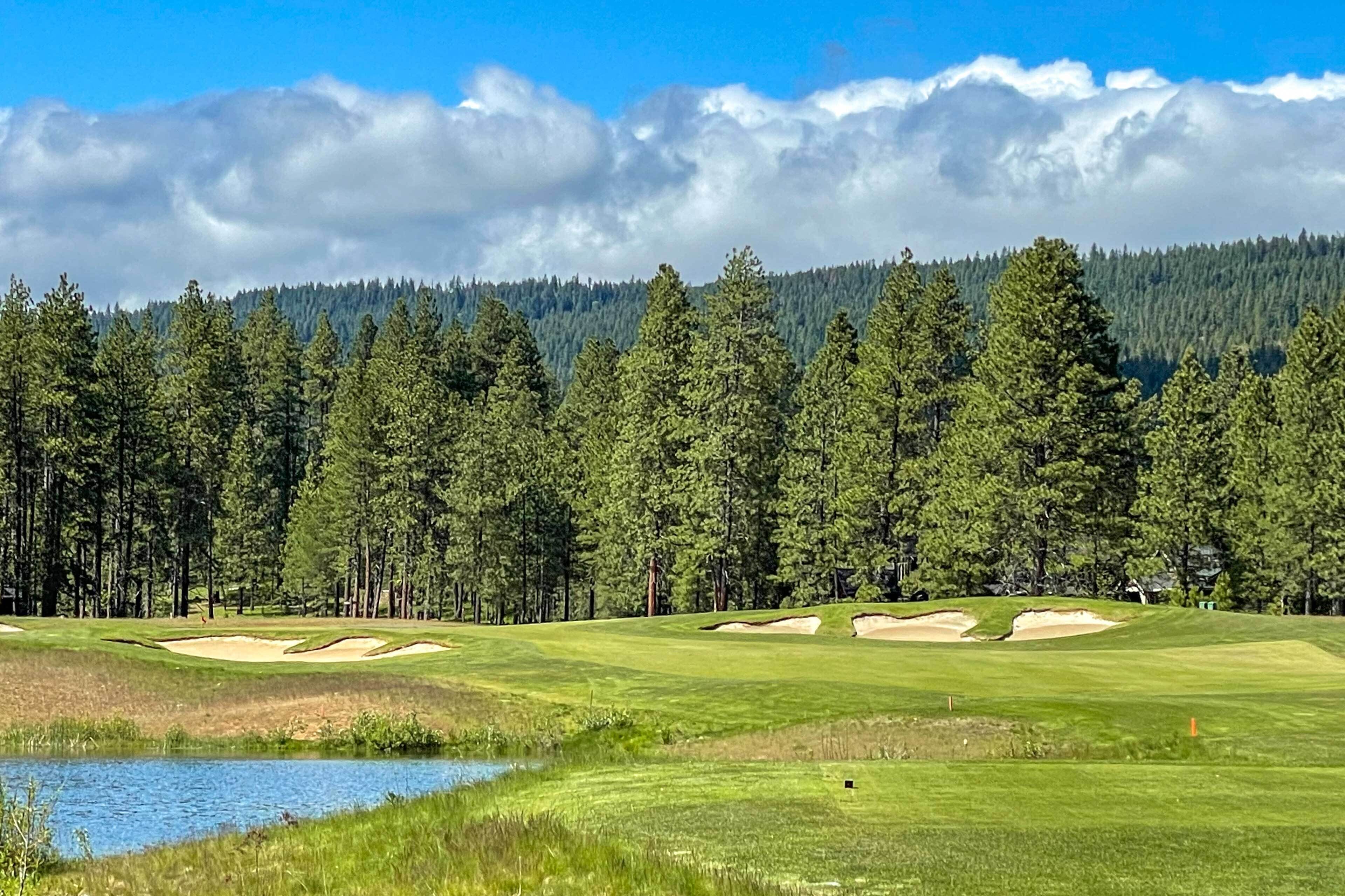 Golfkenttä, jossa on hiekkabunkkereita, vesialue ja metsäinen tausta.