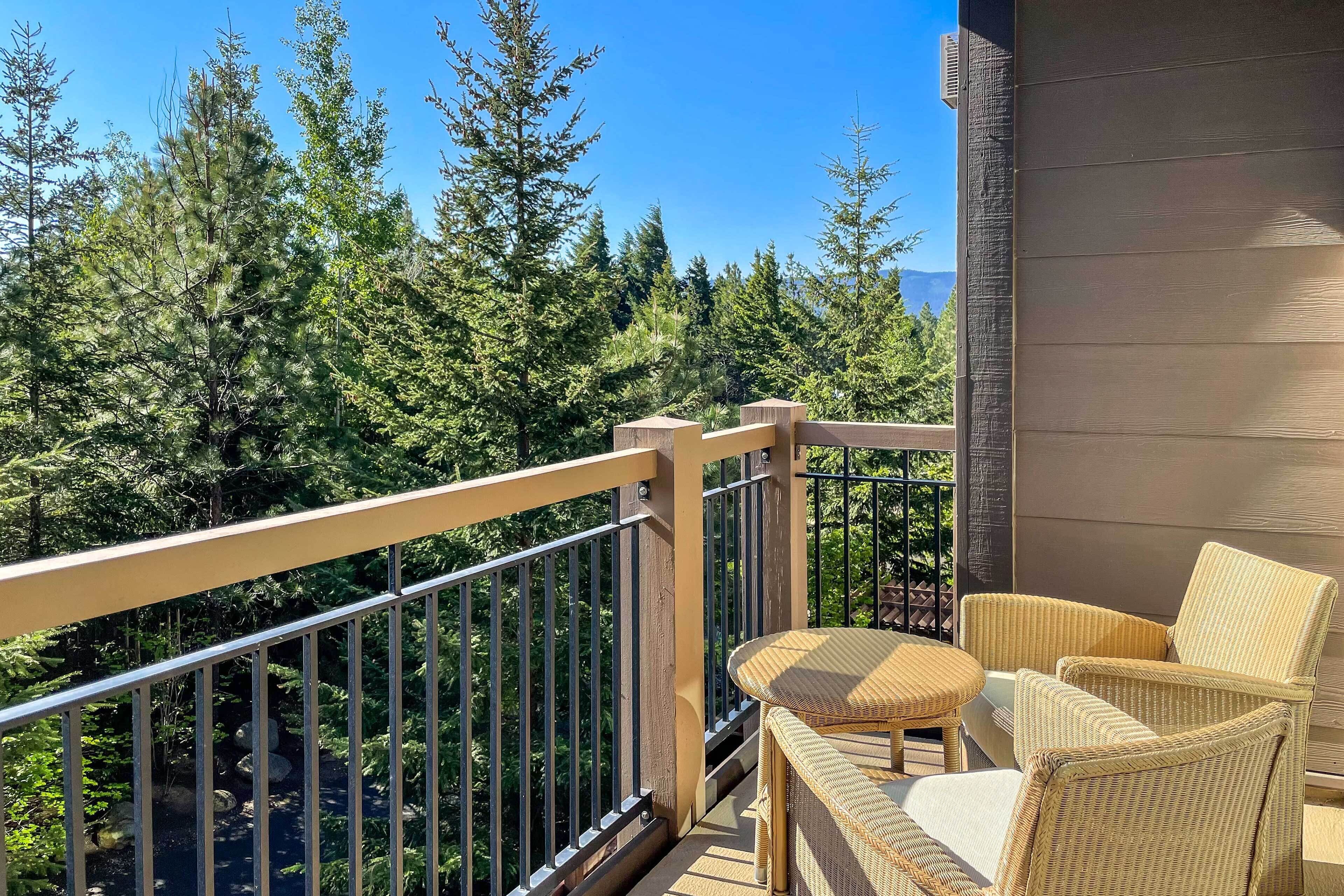 Un balcon agrémenté de meubles en osier, une vue sur une forêt dense et un ciel bleu dégagé.