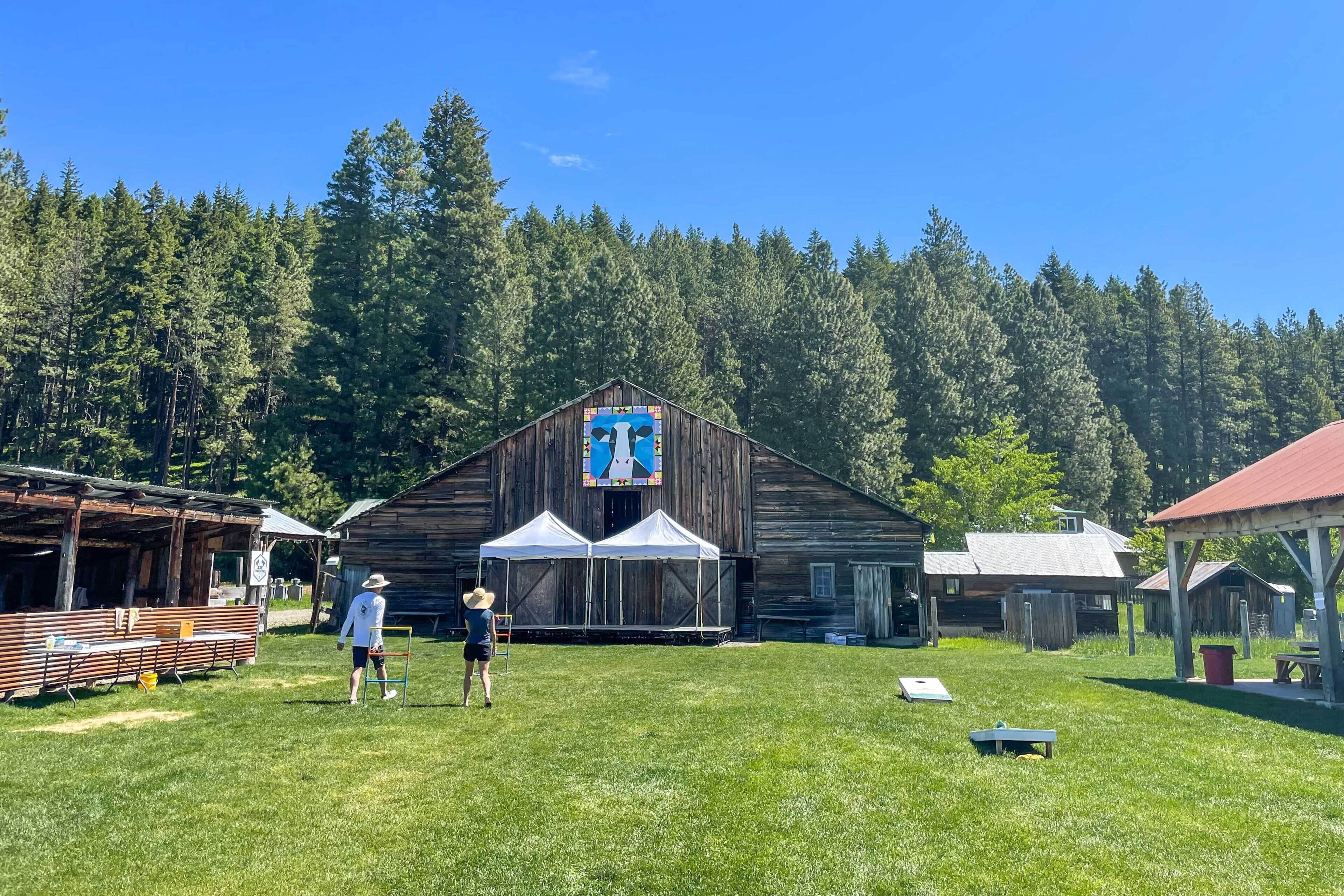 A rustic wooden barn with a large stained glass window, surrounded by a grassy field and dense forest.