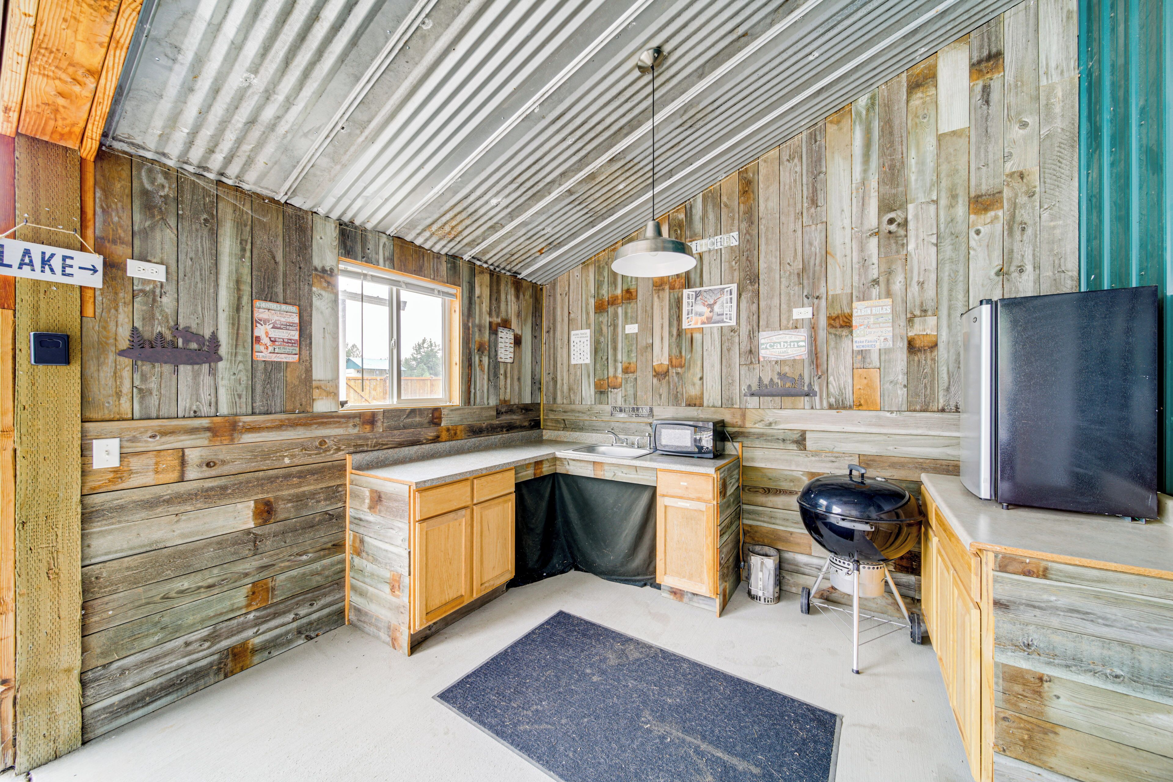 A rustic cabin with a wooden interior, a sink, a refrigerator, and a grill.