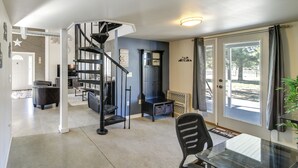 A modern kitchen with a black spiral staircase, a dining area with a glass table, and a view through a glass door.
