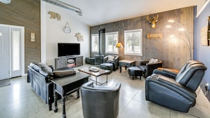 A modern living room with a fireplace, leather sofas, a flat-screen TV, and a mounted deer head.