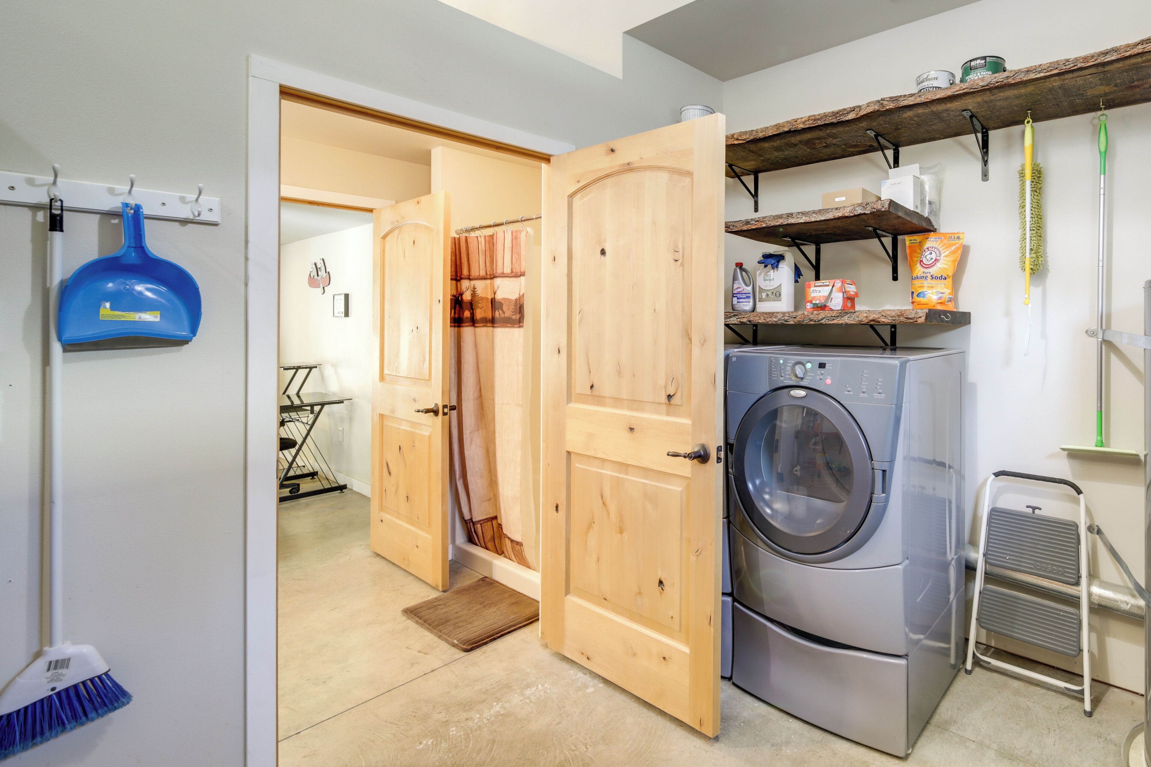 A laundry area with a washing machine, wooden doors, a broom, and shelves with cleaning supplies.