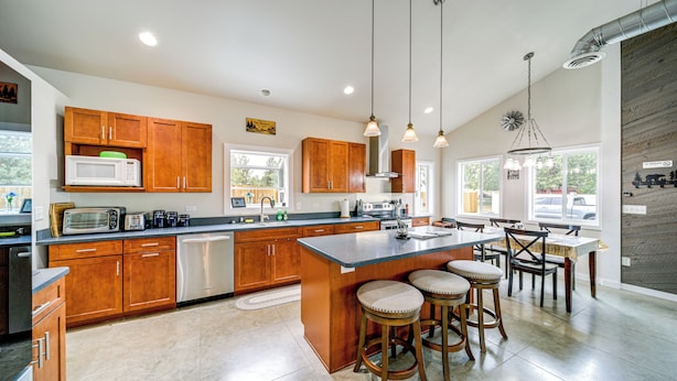 A modern kitchen with wooden cabinets, a large island with stools, and pendant lighting.