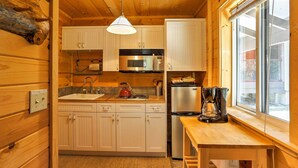 A compact kitchen with wooden cabinets, a microwave, a refrigerator, a coffee maker, and a window providing natural light. - Romantic Riverfront Cottage - 1 Mile to Winthrop! (Winthrop)