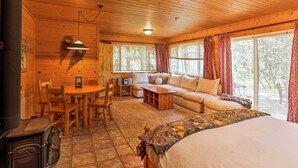 A cozy cabin interior with a wooden ceiling, a sofa, a dining table, and a fireplace. - Romantic Riverfront Cottage - 1 Mile to Winthrop! (Winthrop)