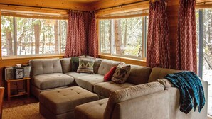 A cozy living room with a sectional sofa, ottomans, and a small table with speakers. - Romantic Riverfront Cottage - 1 Mile to Winthrop! (Winthrop)