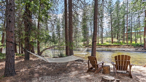 A hammock between trees, two Adirondack chairs, and a log fire pit in a forested area by a river. - Romantic Riverfront Cottage - 1 Mile to Winthrop! (Winthrop)