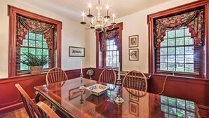 A dining room with a wooden table, chairs, a chandelier, and windows with floral curtains. - Beautiful Historic House In Amish Country (Ephrata)