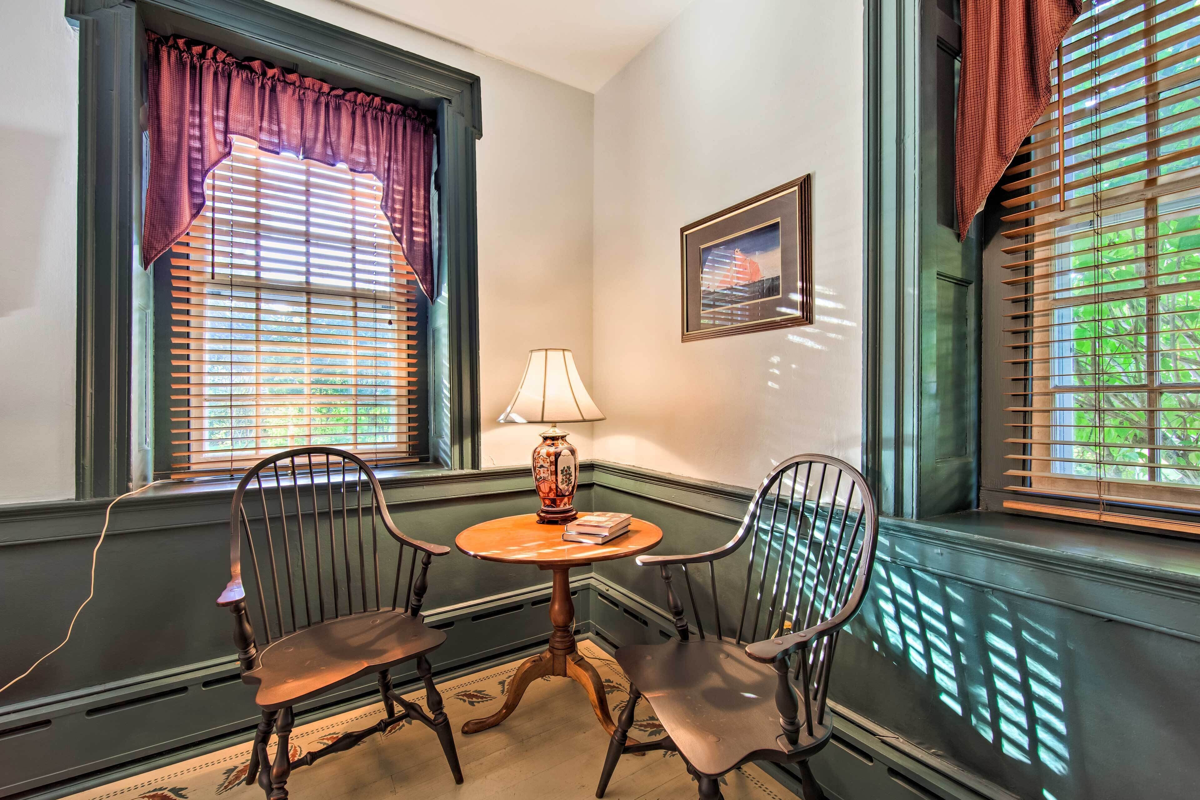 A corner room with two chairs, a small round table, a lamp, and a framed picture on the wall.