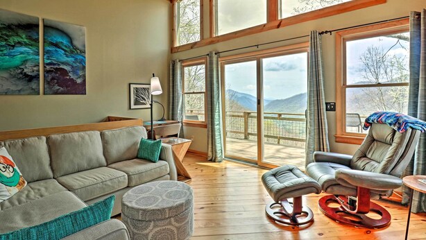 A spacious living room with a sofa, ottoman, and recliner, large windows with a view of mountains, and artwork on the walls. - Serene 'mountain Mist' Retreat w/ Deck & Hot Tub! (Maggie Valley)