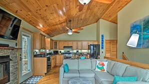 A spacious living area with a grey sectional sofa, a ceiling fan, and a stone fireplace. - Serene 'mountain Mist' Retreat w/ Deck & Hot Tub! (Maggie Valley)