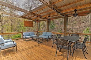 A covered outdoor deck with wooden flooring, blue cushioned seating, and metal tables and chairs. - Serene 'mountain Mist' Retreat w/ Deck & Hot Tub! (Maggie Valley)