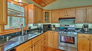 A kitchen with wooden cabinets, a stainless steel sink, a microwave, a stove, and a coffee maker. - Serene 'mountain Mist' Retreat w/ Deck & Hot Tub! (Maggie Valley)