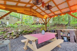 An outdoor covered patio with a checkered tablecloth, picnic benches, and a grill area. - 'lotsa Moose Lodge' Pisgah Forest Waterfall Cabin! (Burnsville)