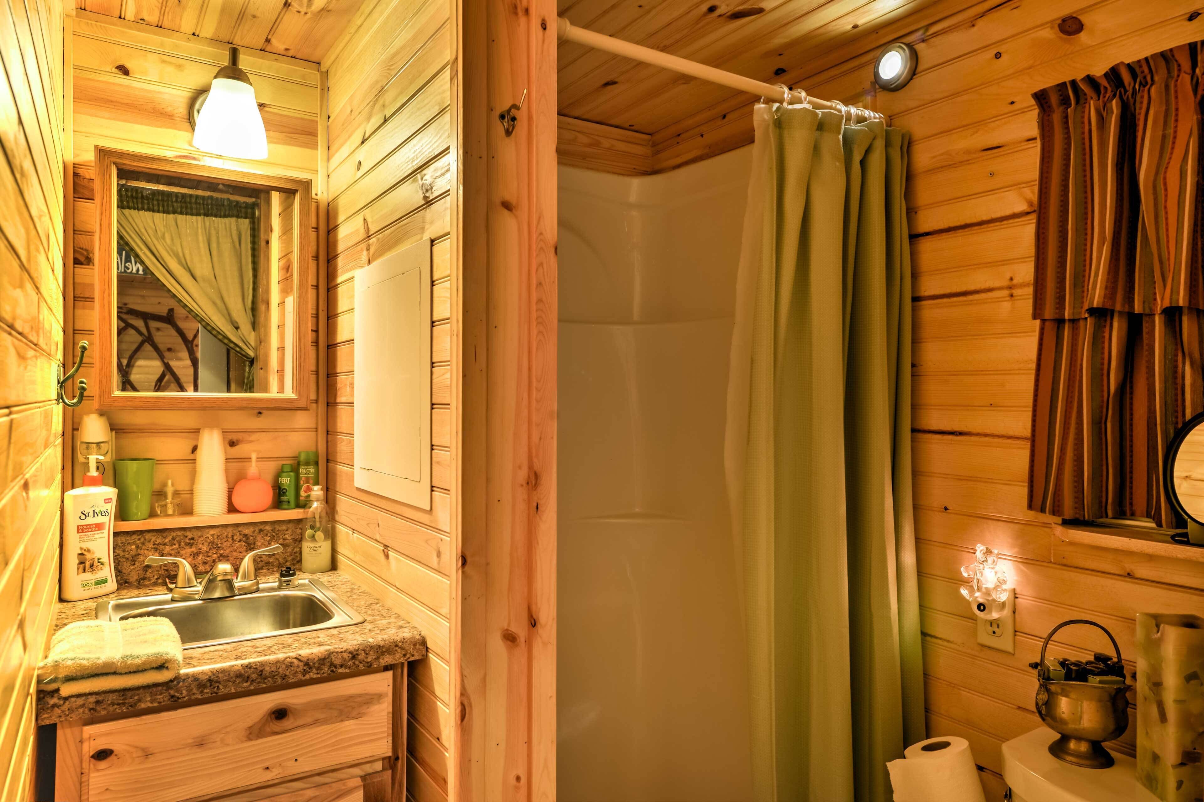 Baño de cabaña de madera con lavamanos, espejo, cortina de ducha y estante con artículos de tocador.