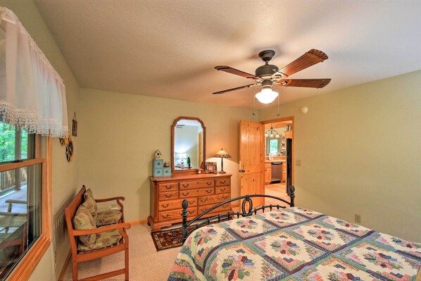 A bedroom with a bed, a wooden dresser, a chair, a ceiling fan, and a window.