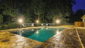 A swimming pool with stone tiles, surrounded by a fence and trees, with lights illuminating the area. - 18 Mi to Dtwn Memphis: Oasis on 8 Acres! (Southaven)
