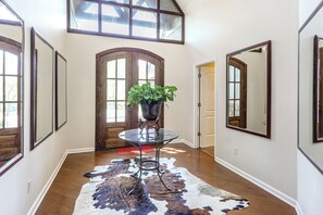 A hallway with a glass table, a potted plant, a cowhide rug, and a wooden door.