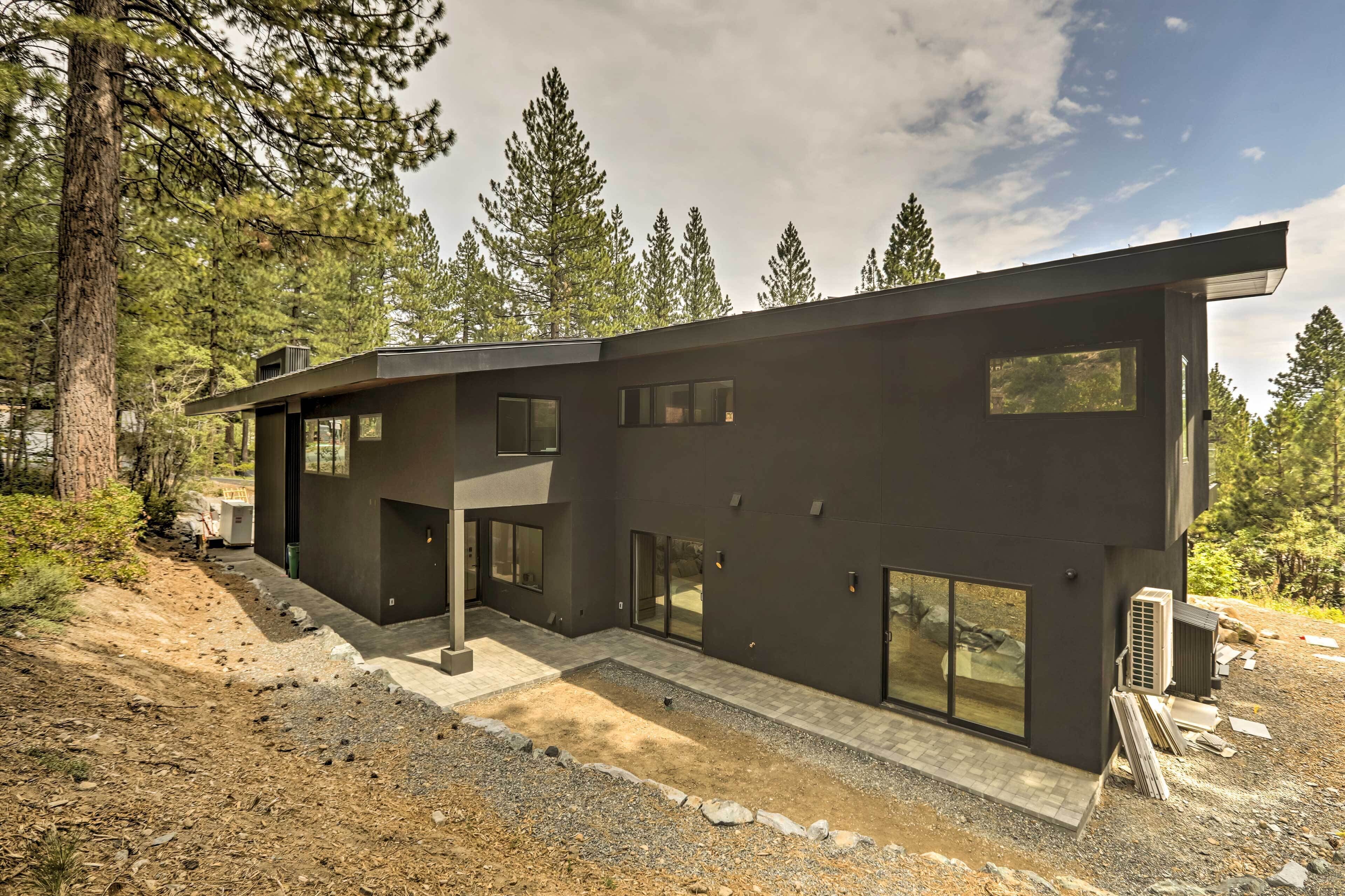 A modern two-story house with large windows and a flat roof, surrounded by trees.