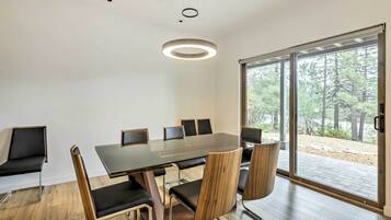 A modern meeting room with a glass table, wooden chairs, and a view of a forest through large windows.