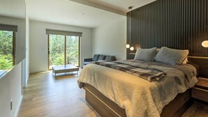 Ein modernes Schlafzimmer mit einem großen Bett, einer Sitzbank und Blick ins Grüne durch das Fenster.