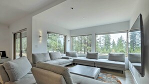 Ein modernes Wohnzimmer mit einem Ecksofa, einem Couchtisch und einem großen Fenster mit Blick auf Bäume.