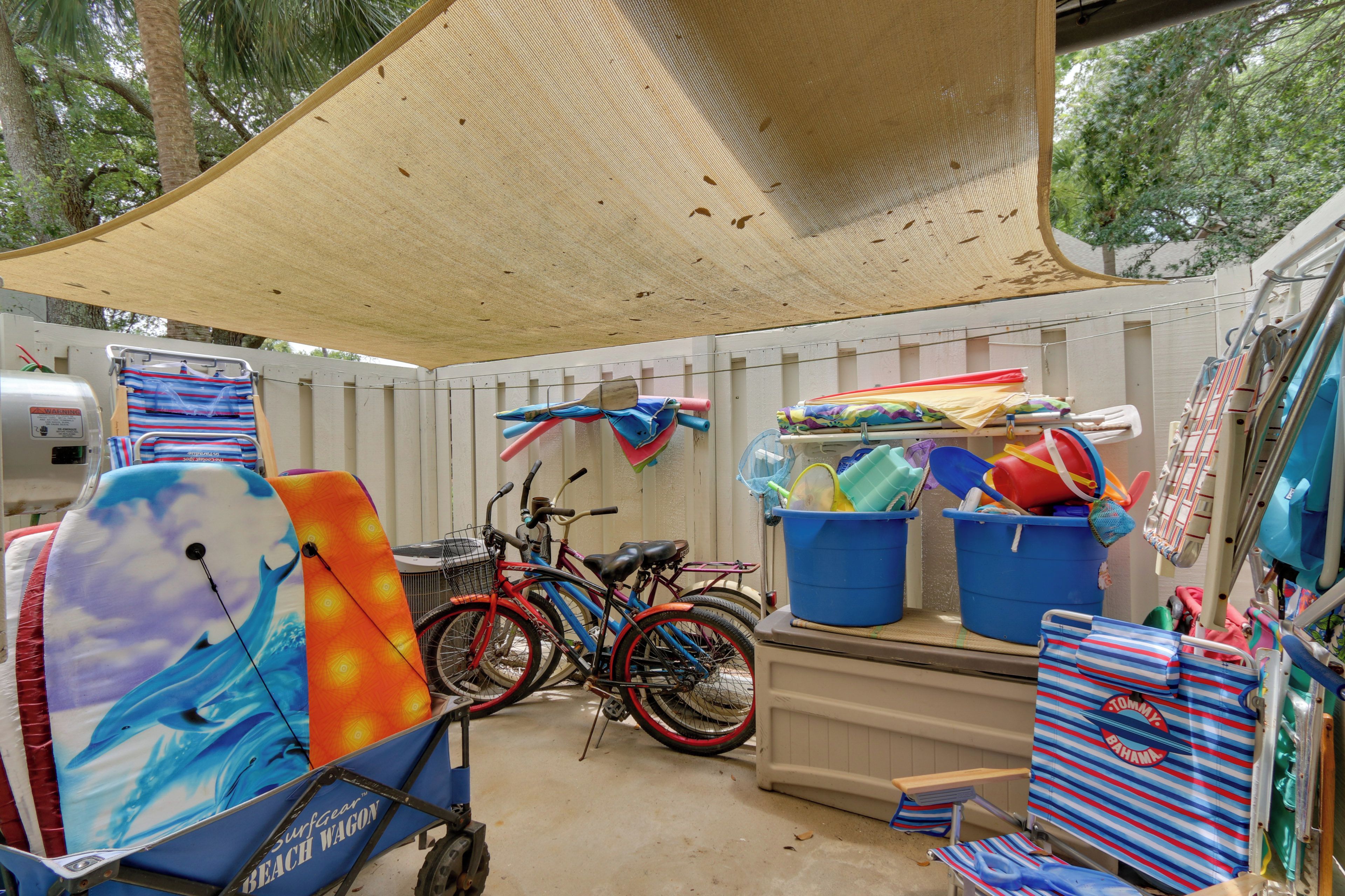 Ein überdachter Außenbereich mit Strandutensilien, darunter Surfbretter und Fahrräder.