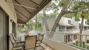 Un balcon avec une table et des chaises, un espace abrité et une vue sur les bâtiments et les arbres voisins.
