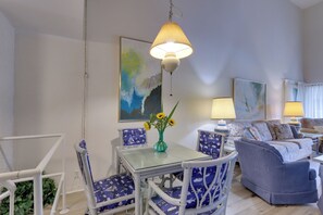 Una sala de estar con un sofá, una mesa de comedor con sillas, una lámpara colgante y un cuadro en la pared.