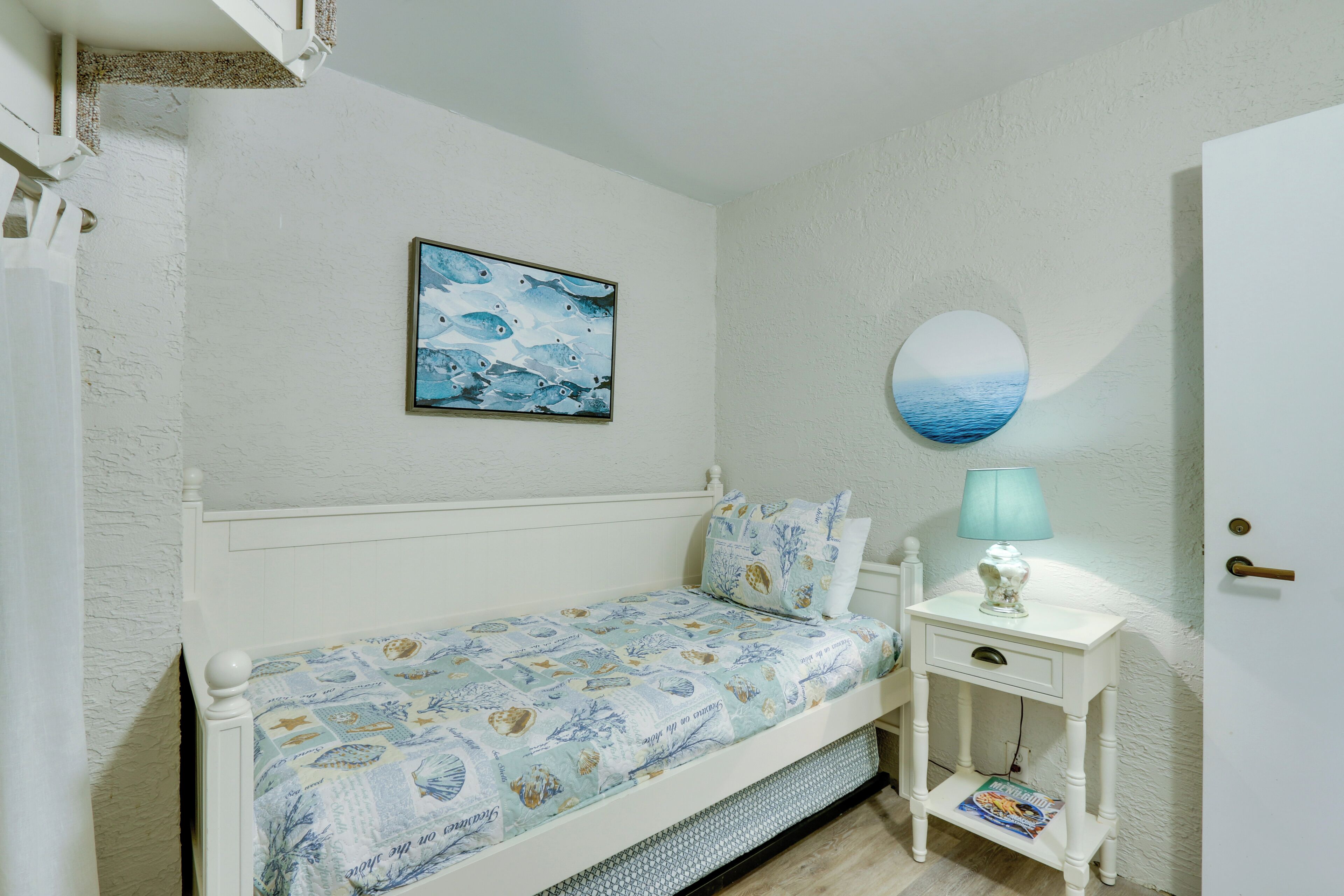 Een slaapkamer met een bed, een nachtkastje met een lamp, een aan de muur hangend schilderij en een deur.