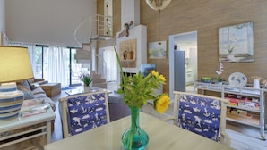 Un vaste salon avec un escalier, un coin repas agrémenté d’un vase de fleurs et une cuisine visible au fond.
