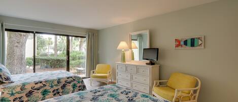 A hotel room with two beds, a dresser, a television, and a chair.