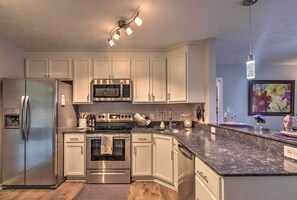 A modern kitchen with white cabinets, stainless steel appliances, a granite countertop, and a pendant light.