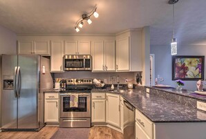 Una cocina moderna con electrodomésticos de acero inoxidable, armarios blancos, encimera de granito y una lámpara decorativa.