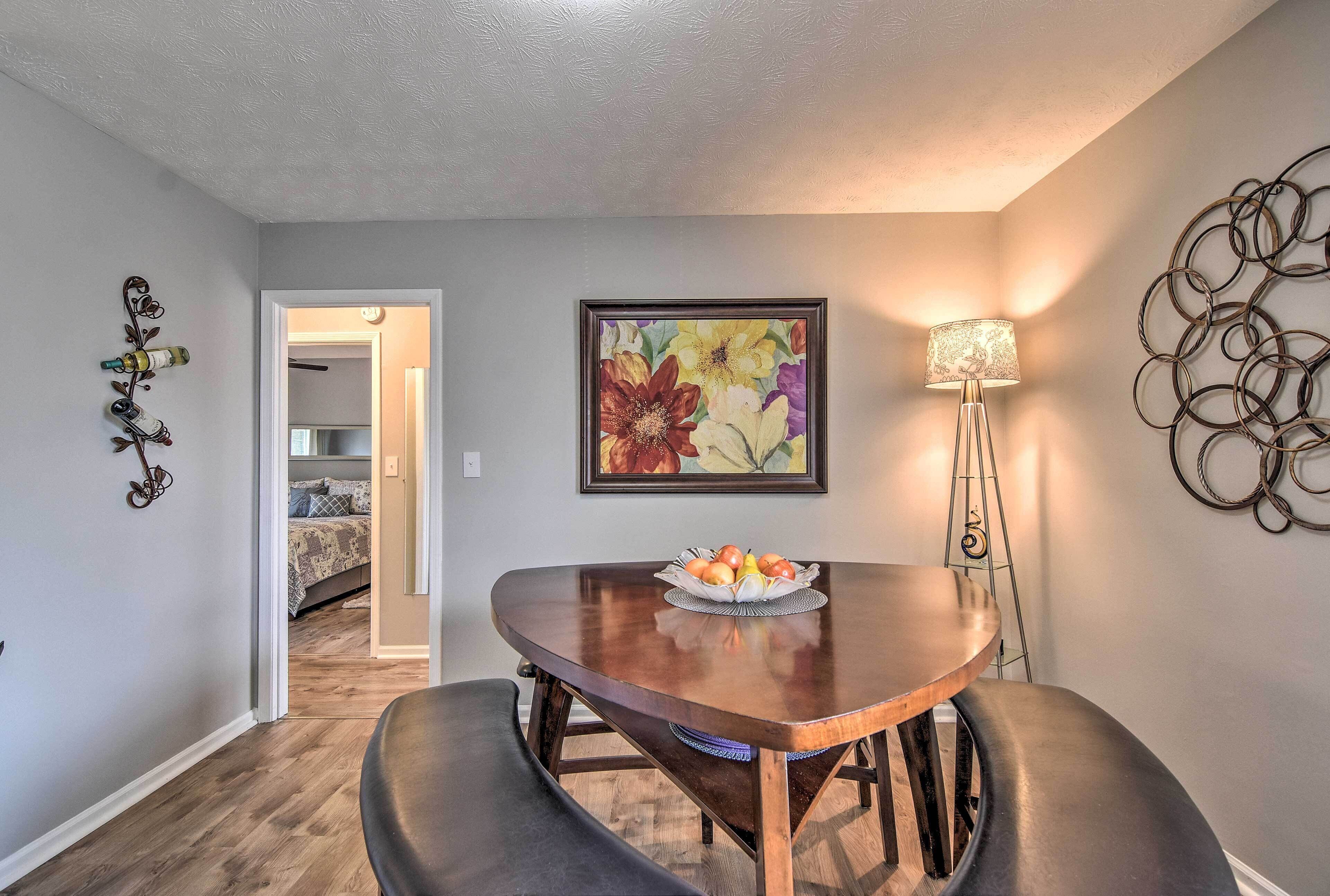 A dining area with a wooden table, a fruit bowl, a lamp, and a painting on the wall.