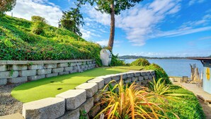A golf course with a stone retaining wall, a large tree, and a view of the water.