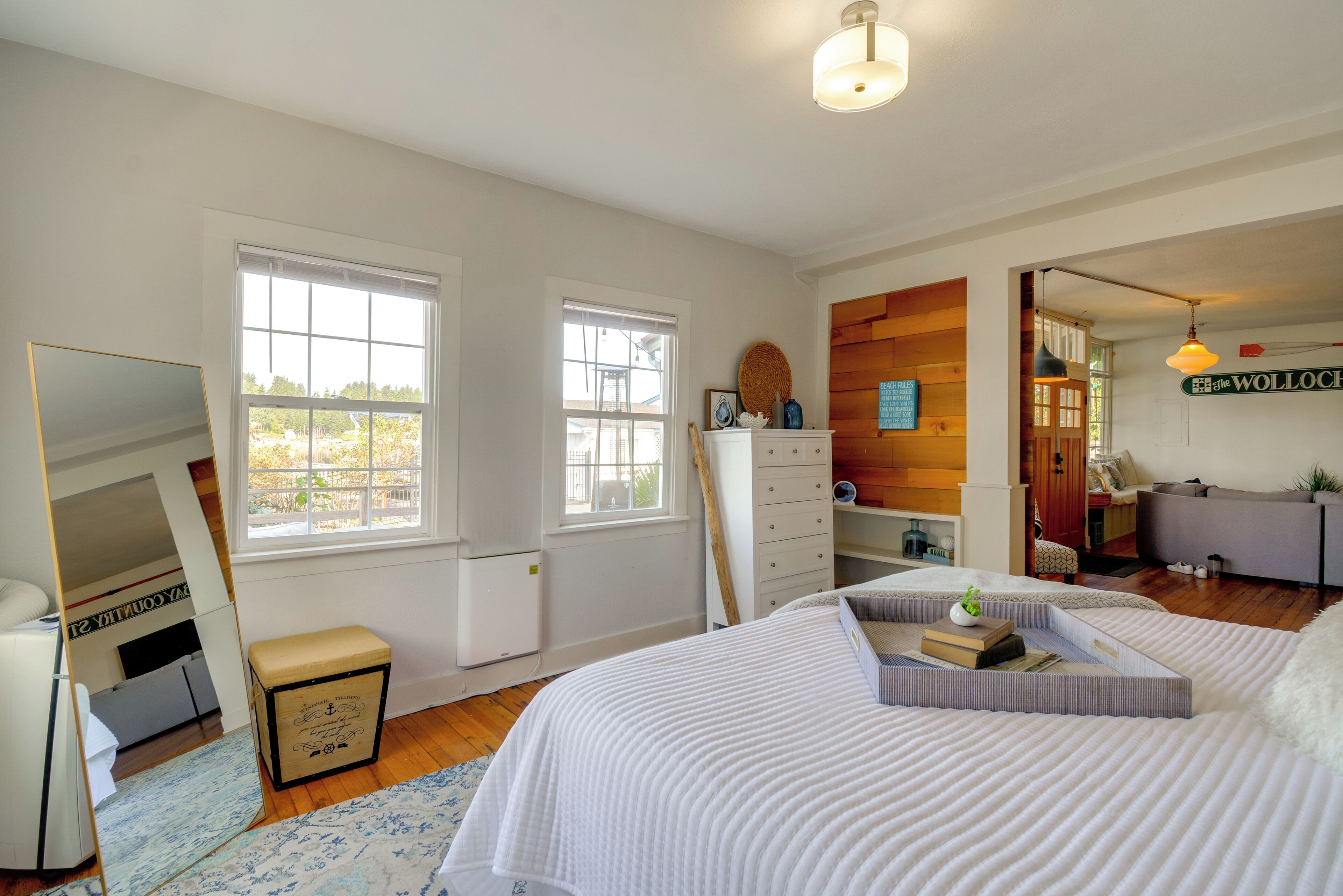 A bedroom with a bed, dresser, and a mirror. There are two windows and a door.