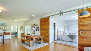 A spacious living area with a wooden floor, a dining table with chairs, a sofa, and a large wooden door.