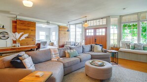 A spacious living room with a large sectional sofa, a wooden accent wall, and a bay window with a view of greenery.