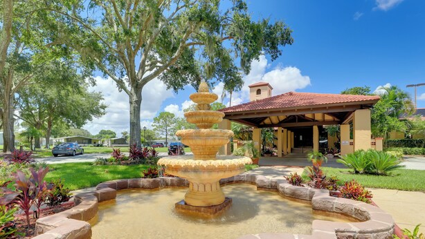 A fountain surrounded by stone steps and greenery, with a building in the background. - Steps to Pool: Winter Garden House w/ Lanai! (Winter Garden)