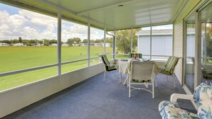 A covered patio with a view of a green field, white chairs, a table with plates and cups, and a blue carpet. - Steps to Pool: Winter Garden House w/ Lanai! (Winter Garden)